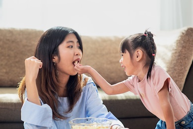 happy asian child enjoy eating popcorn with her older sister, love and happiness family concept