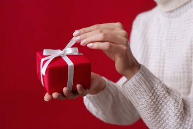 female hands open christmas red gift box with white bow on the red background. white sweater. new year concept. winter holidays and presents. surprise delivery. unpacking. valentine's day, birthday