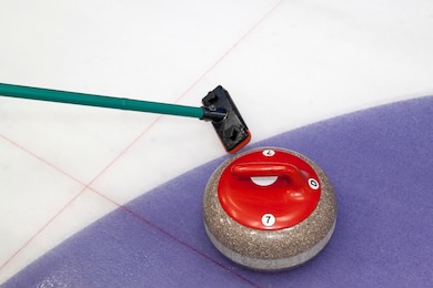 broom and stone for curling. view of red curling stone in outer blue ring of house with broom nearby