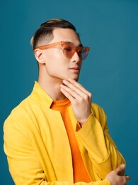 a guy with glasses on a blue background touches his face with his hand and looks to the side
