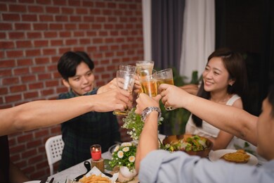group of asian friends clink glasses of beer at a party. they are very happy and have fun.