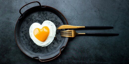 banner.homemade fried egg in a vintage pan and stylish cutlery on a dark background. heart-shaped yolk.view from above. copy space for text.