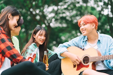 group of happy asian young people sitting on the guitar and singing in the park

