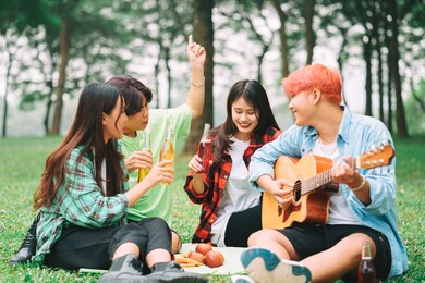 group of happy asian young people sitting on the guitar and singing in the park
