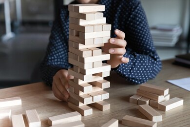 close up indian businesswoman building tower from wooden blocks in office, playing game, sitting at work table, employee planning future, developing project or business strategy, making decision