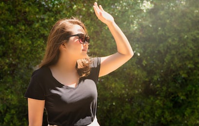 a young beautiful asian woman wearing 100% uv light eyes protection sunglasses, stand and raise her hand to block out bright glare and sunlight. ultraviolet rays, over exposure. sunscreen, skincare.