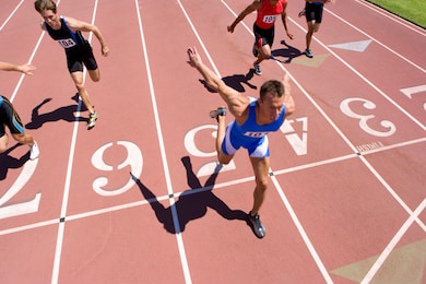 young male sprinter stepping over the finishing line while his competitors are behind him on a bright, sunny day at an athletics event