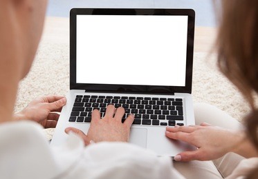 beautiful young couple sitting side by side on a sofa looking at a laptop together