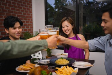 group of asian people are celebrating the festival. they clink glasses of beer and eat.