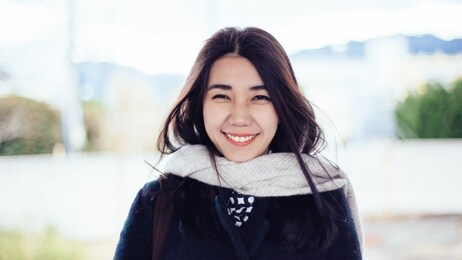 asian woman traveler smile and laughing in warm clothes in winter. college student female teenager smiling looking at camera with a positive friendly smile in blur blue and green background outdoor 