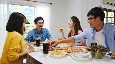 happy young friends group having lunch at home. asia family party eating pizza food and laughing enjoying meal while sitting at dining table together at house. celebration holiday and togetherness.