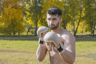 a young mixed martial artist in fighting gloves stands in a boxing stance against the background of an autumn landscape and looks into the camera.