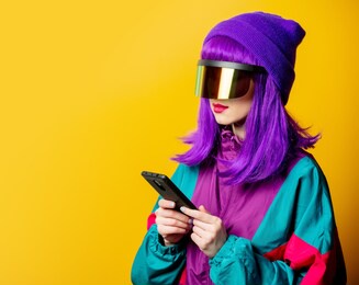style woman in vr glasses and 80s tracksuit with mobile phone on yellow background