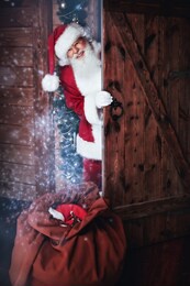 merry christmas and happy new year! santa claus comes in a wooden house from the cold with a bag of presents and smiles.