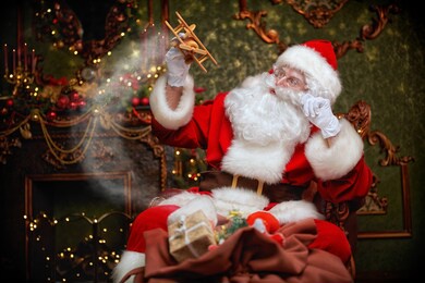 santa claus brought gifts for christmas. he sits in an armchair in a beautiful christmas interior and plays with a wooden airplane. christmas and new year concept. 
