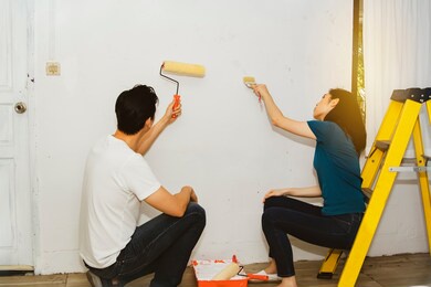 
asian couple working hard to paint the interior walls of their home in a refurbishment process.