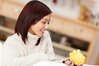 young asian woman looking at her piggy bank with a dreamy expression as she imagines realising her goals with her savings