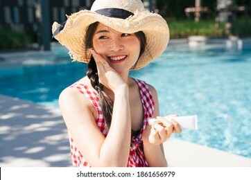 beautiful asian woman in pink dress applying sunblock lotion near swimming pool.