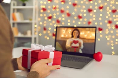 video call on saint valentine's day. couple sending each other love and showing presents on virtual date. closeup of man's hands holding gift box. shimmering yellow lights, soft focus, selective focus