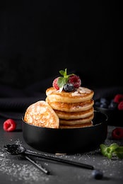 small thin pancakes with fresh berries and honey in a black bowl, close-up