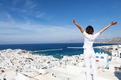 rear view of young woman with arms outstretched, looking at the cityscape of mykonos island, greece. copy space.