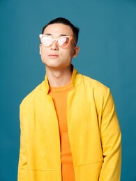 portrait asian man wearing glasses orange tshirt yellow jacket blue background cropped view model