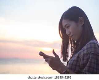 striped shirt woman holding a phone by the sea