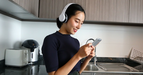 asian women wearing headphone and listening to music in the kitchen at home