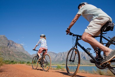 low-angle shot of an elderly woman mountain biking with her husband along a pathway by the lake at the countryside.
