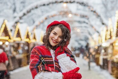 winter, christmas, new year holidays concept: happy smiling woman posing at street festive market. model wearing red beret, tartan scarf, red gloves, white knitted sweater. copy, empty space for text