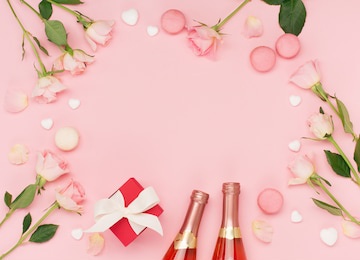 festive holiday greeting card for valentines, birthday, woman or mothers day. flowers, bottle of wine, sweets and gift on pink background. valentines day concept. flat lay, top view, copy space.