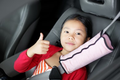 asian child cute or kid girl smile sit and wearing seatbelt or safety belt with pink soft cover on seat for safe in car or vehicle with thumb up to like or good for transport holiday travel