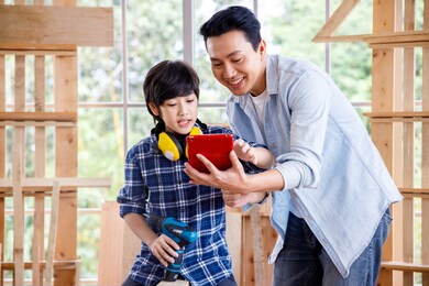 asian father and son looking at digital tablet in carpentry workshop at home.
