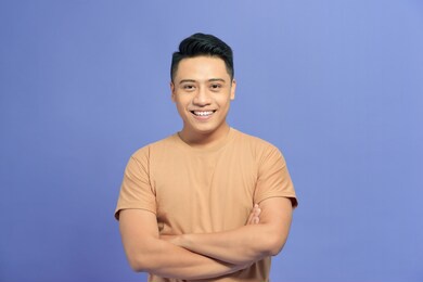 smiling handsome asian man in casual brown t-shirt with arm crossed isolated on color background 