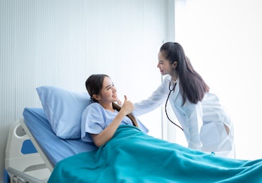 asian young female patient on bed showing thumbs up with smiley face very good symptom to asian young female doctor in hospital background.