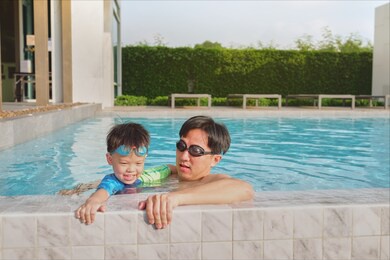 asian father holding cute little asian toddler boy child on the edge of a swimming pool, little kid takes a swimming lesson with his parent, happy dad and son spending time together