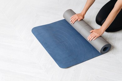 close up woman hands preparing fitness equipment for yoga or workout class at home or in sport gym. woman finished or starting yoga class rolling exercise mat. wellbeing concept. copy space