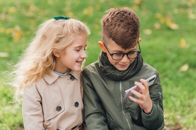 little boy and girl watching video on smartphone while resting in park on weekend day together