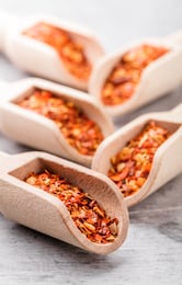 dried chili peppers flakes in wooden scoops on rustic gray background selective focus overhead vibrant color close up arrangement studio shot