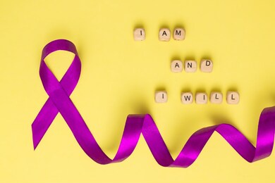 wooden cubes with text of the slogan of world cancer day i am and i will and a purple ribbon on a yellow surface