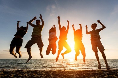 multiracial group of people jumping at beach, backlight