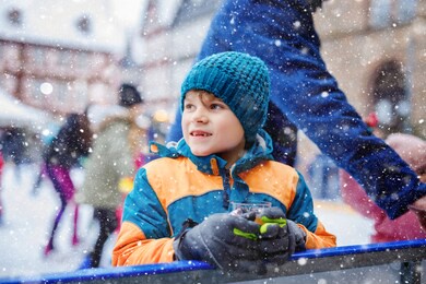 happy little kid boy in colorful warm clothes on skating rink of christmas market or fair drinking hot punch or chocolate. healthy child having fun on ice skate. people having active winter leisure