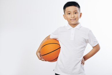 portrait of cheerful asian preteen boy posing with basketball ball and looking at camera