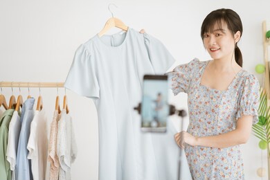 young asian beautiful woman is using her smartphone to live stream to sell clothes on social media platforms and e-commerce sites. this will be the future trend of the ecommerce industry
