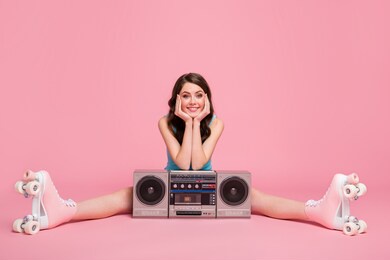 full size photo of young happy smiling girl hold hands face sit floor boombox in rollers isolated on pink color background