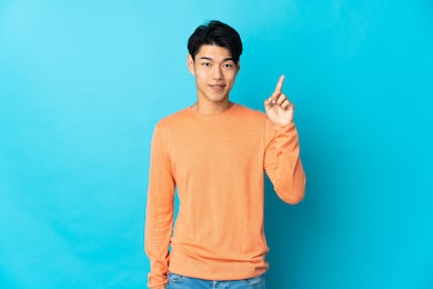 young chinese man isolated on blue background showing and lifting a finger in sign of the best