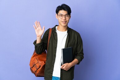 young student woman isolated on purple background saluting with hand with happy expression