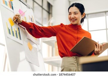 casual creative happy smile asian business woman planning strategy analysis putting post it stickers note to share idea for startup project on glass board at modern office