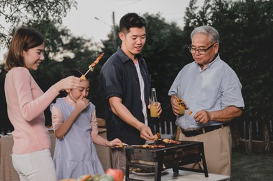 asian family having a barbecue party at home. cooking grilled bbq for dinner in backyard. lifestyle on summer holiday.