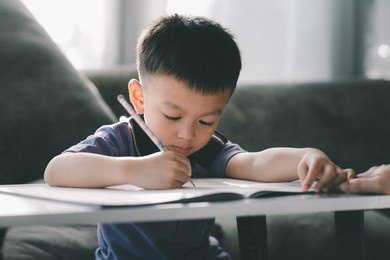 asian boy doing homework with the intention. child boy holding pencil writing, a boy drawing on white paper at the table, elementary school and home schooling, distance education concept.